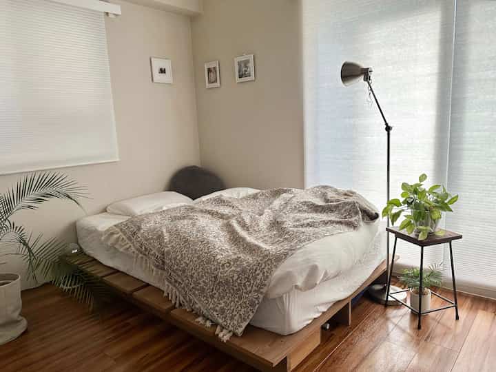 やわらかなホワイトとナチュラルな木目調の寝室、フレンチスタイルのパターンのマルチカバーとフロアランプが配置された雰囲気のあるインテリア