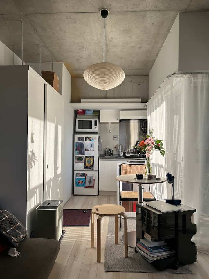 A white and natural tone studio apartment featuring a cozy sofa, dining table, and pendant light setting a warm single household atmosphere
