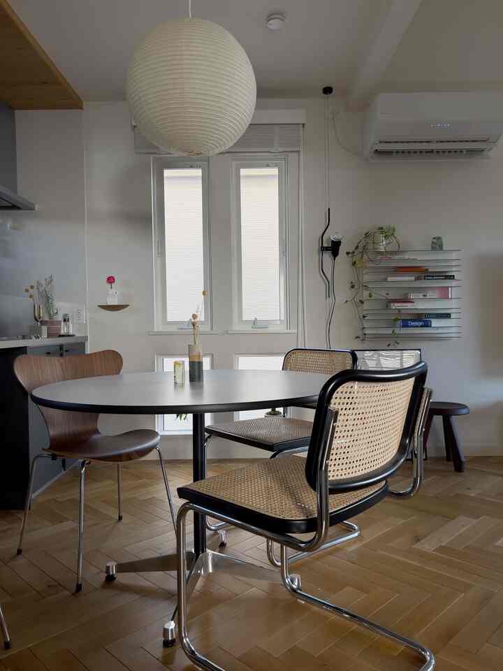 Simple and natural dining room with white walls and wood-tone herringbone flooring, featuring a black dining table and rattan chairs