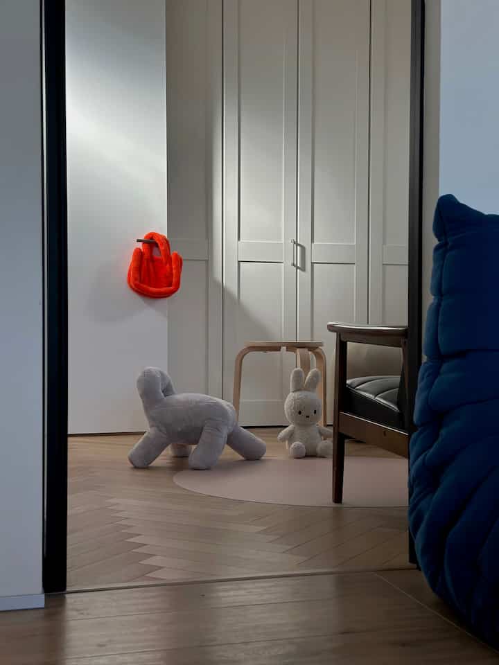 白い壁とナチュラルな木目調床の子供部屋、パステルピンクのラグと小さなスツール、ぬいぐるみが配置された雰囲気のあるインテリア