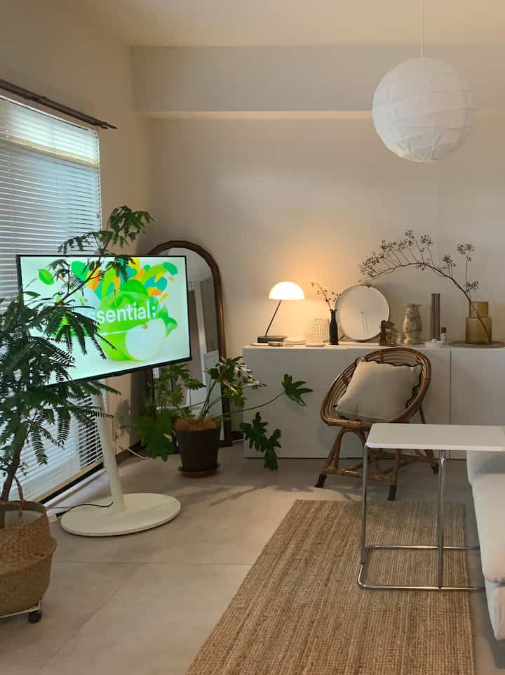 白とナチュラルトーンのリビング、ラタンのアームチェアと植物が配置されたシンプルでモダンな雰囲気のあるインテリア