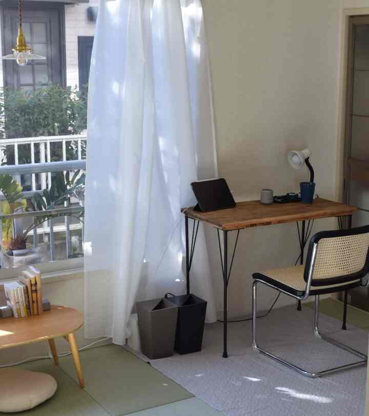 Natural-toned workspace with natural light and white curtains, featuring a wooden desk and rattan chair creating cozy atmosphere