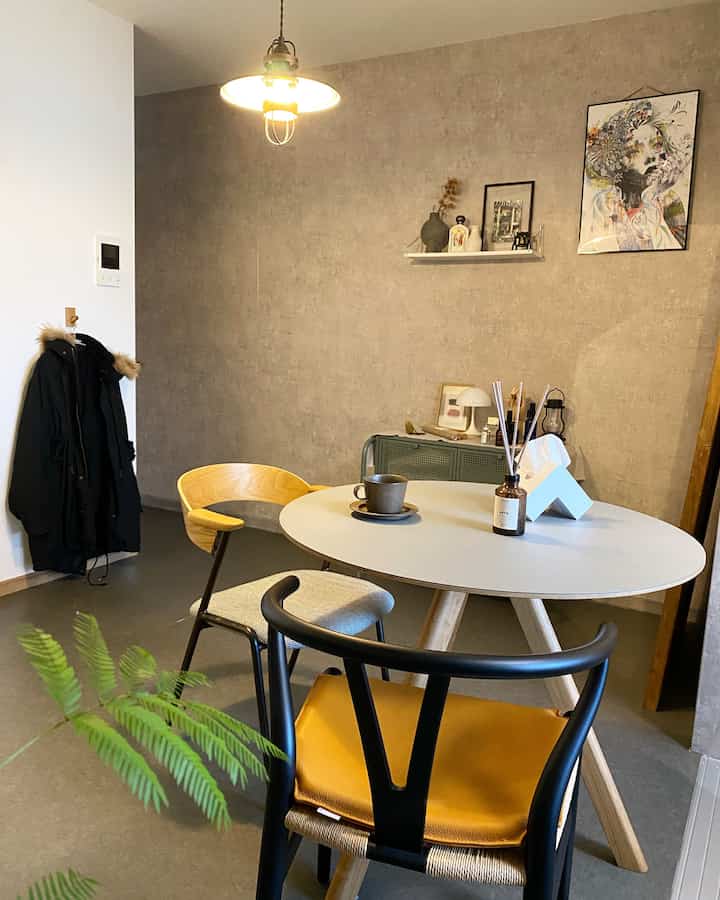 ナチュラルカラーとグレーのトーンが特徴のリビング、ラウンドテーブルと異なるスタイルのアームチェアが配置された雰囲気のある空間