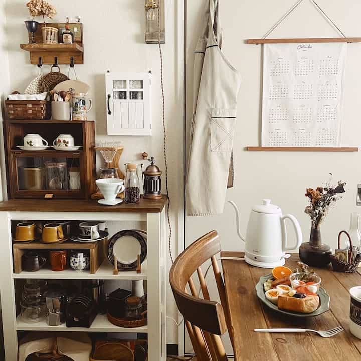 温かみのあるブラウンのキッチン空間、木製ダイニングテーブルとキャビネット、ハンドミルやコーヒー器具が配置されたナチュラルな雰囲気のインテリア