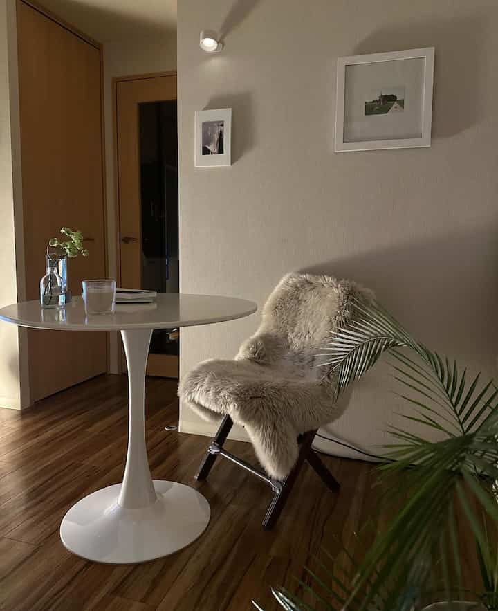 ナチュラルなトーンのワンルームダイニング、白い丸テーブルとムートンラグをかけた椅子が調和するシンプルなインテリア