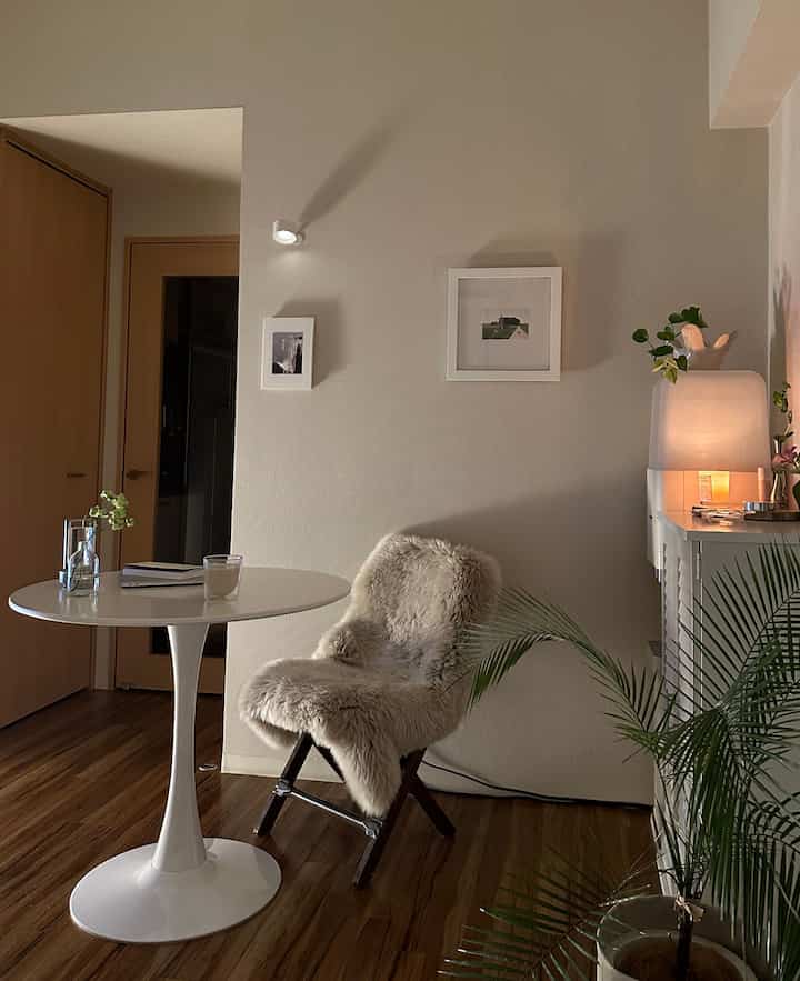 Natural tone living room with soft beige walls and wood flooring, featuring a white round table and a fur-covered chair in a cozy atmosphere