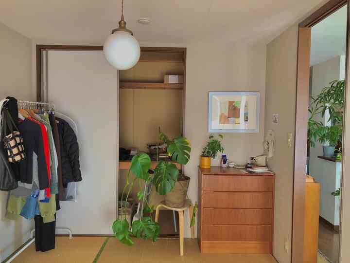 ベージュ色の壁と木目調家具が配置された畳の部屋、衣類ラックとチェスト、植物が置かれた落ち着いた雰囲気のインテリア