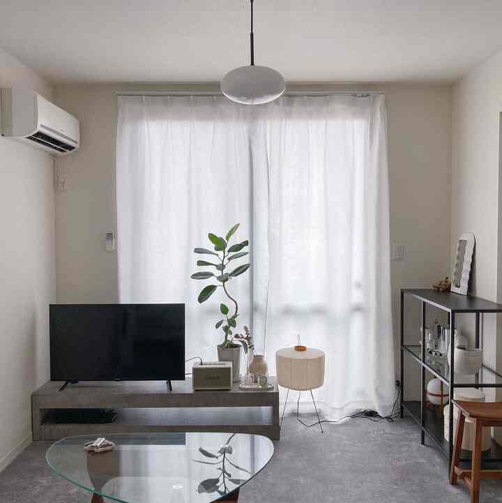 Monotone living room with bright white curtains, glass coffee table, TV, wood stool, and a floor lamp creating a simple, inorganic atmosphere