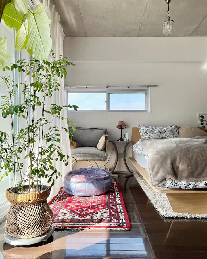 Bright natural light white-toned veranda bedroom featuring wooden bed, side table, and several green plants in a natural setting