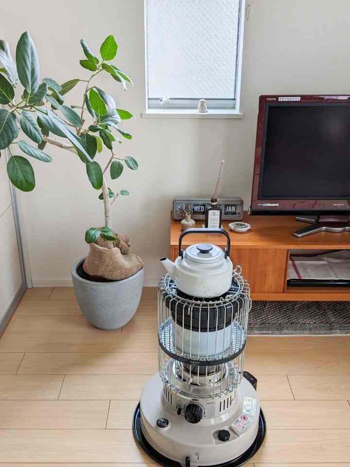 暖かなベージュの床と木目調家具が配置されたリビング、中央に置かれたトヨトミの石油ストーブとケトルが温かな雰囲気を演出する空間