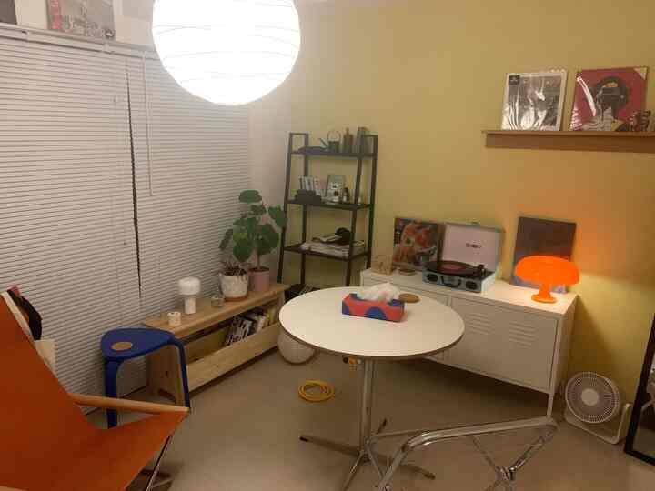 A 1K single household room with yellow wall and white furniture, featuring a round dining table and diverse chairs in a cozy natural interior