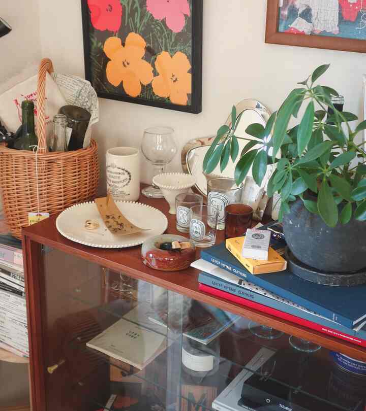 Living room with white walls and brown dresser, featuring plants and assorted objets in a cozy cafe style interior