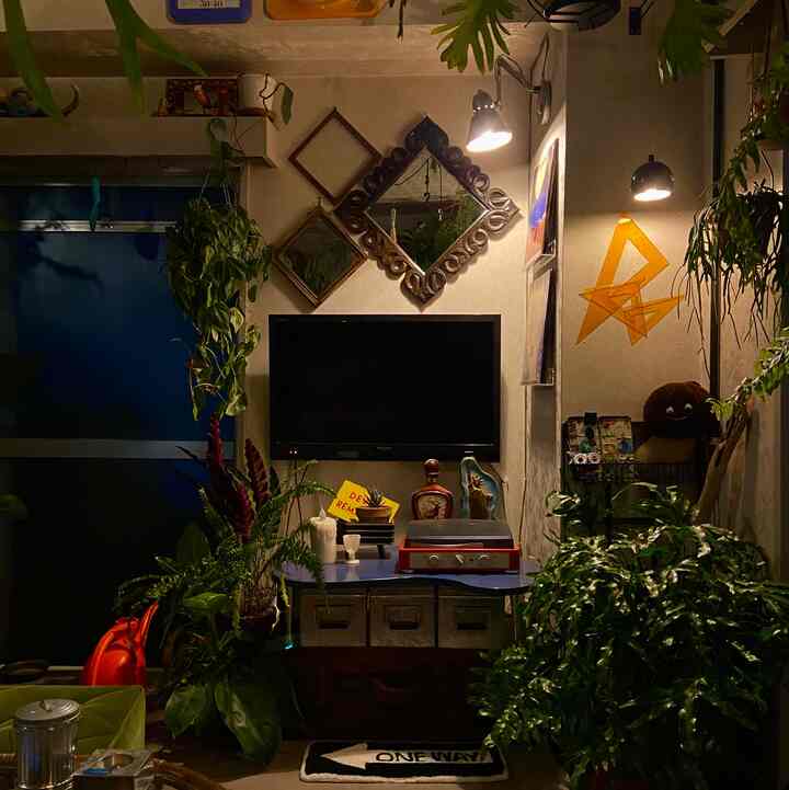 暖かい黄色の間接照明が灯る昭和レトロのリビング、緑の観葉植物とヴィンテージのオブジェが配置された雰囲気のある空間