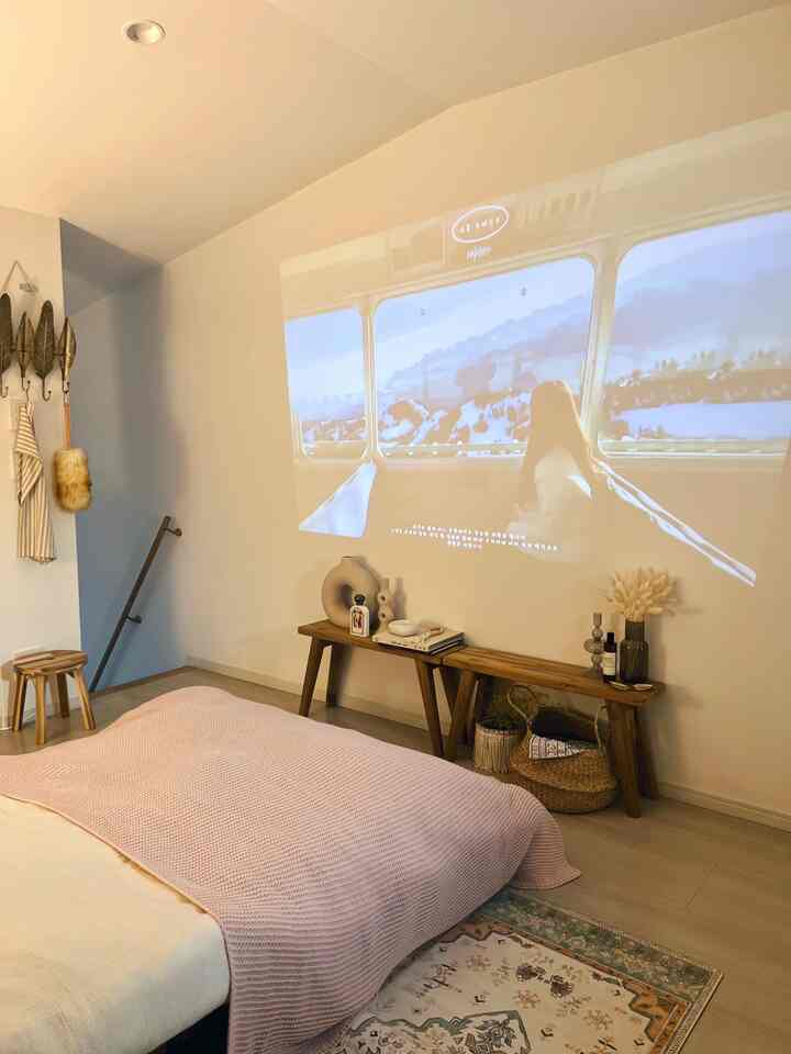 ベージュと木目調が調和した寝室、壁にプロジェクター映像が映されている印象的な一人暮らし用ホームシネマ空間