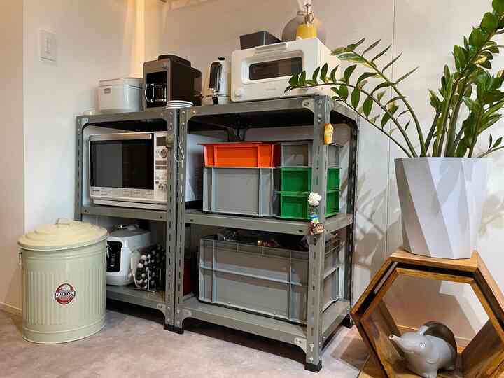 Gray industrial steel shelf in a white-walled kitchen space organized with home appliances and storage boxes, neat and functional atmosphere