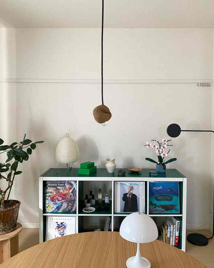 白い壁と緑の棚が調和したダイニング、棚、ランプ、植物が配置された雰囲気のあるインテリア
