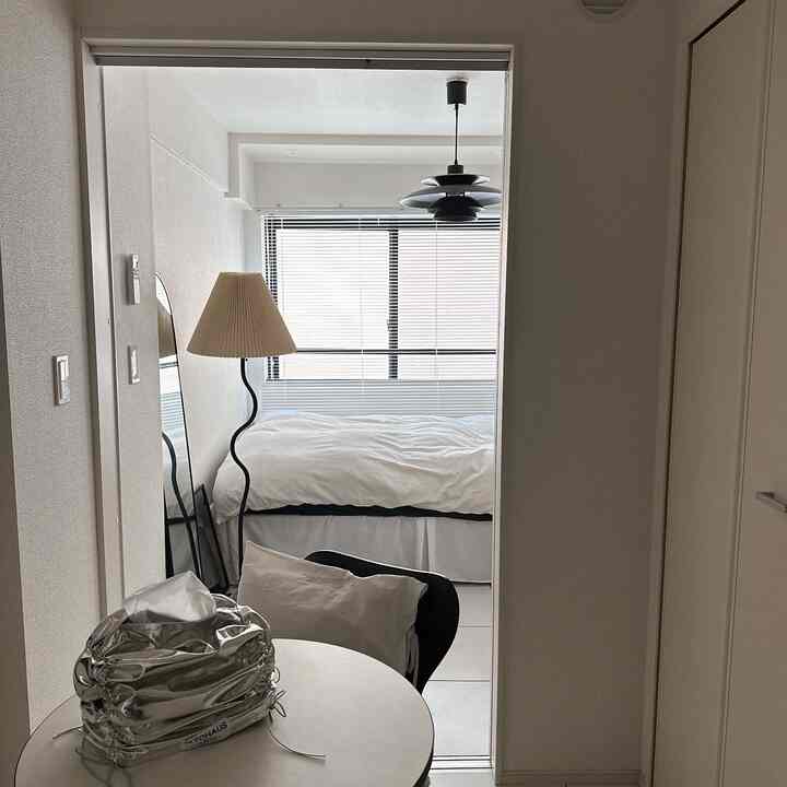 White and beige toned studio bedroom featuring a modern bed, floor lamp, and minimalistic round table with a clean atmosphere