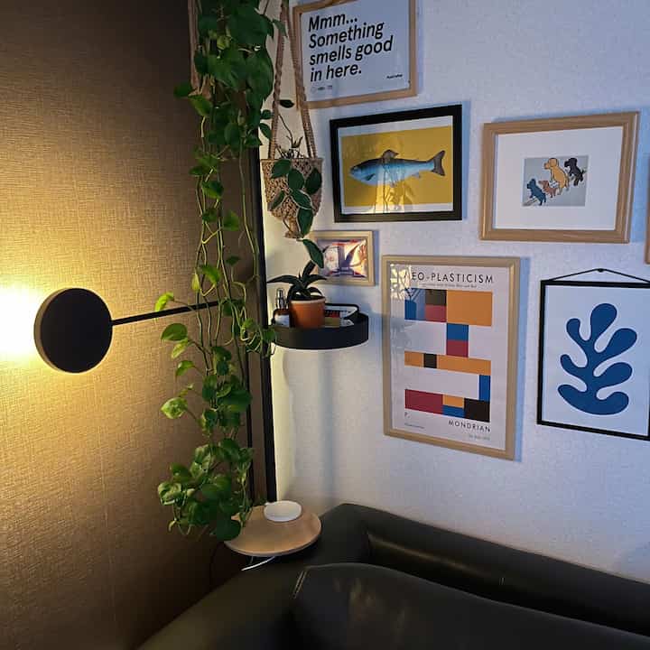 ベージュとブラウンの壁面、黒いソファ、複数の額装アートと植物が配置された落ち着いたコーナーのリビングルーム