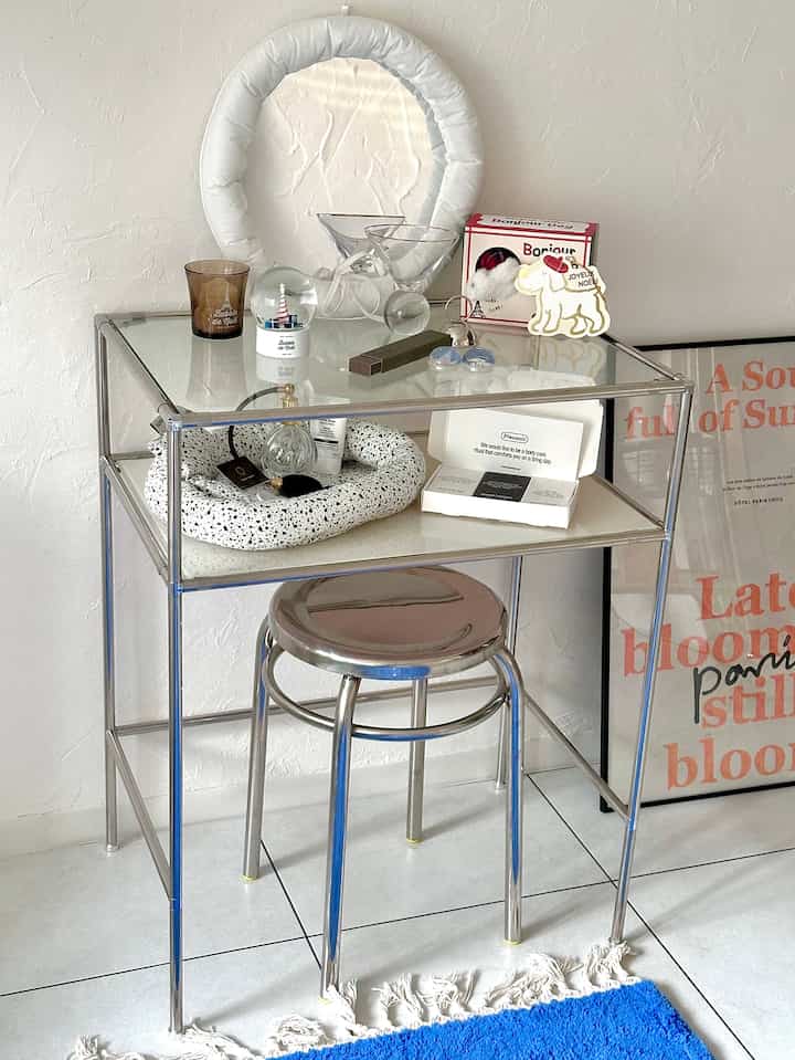 明るい白い壁と透明なガラスのサイドテーブル、シルバーの金属製スツールが置かれたモダンなリビングスペース