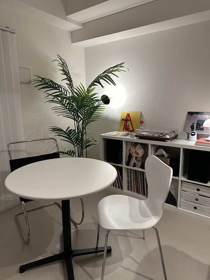 White and green toned Nordic living room featuring round table, chairs, turntable, and decorative plant with cozy atmosphere