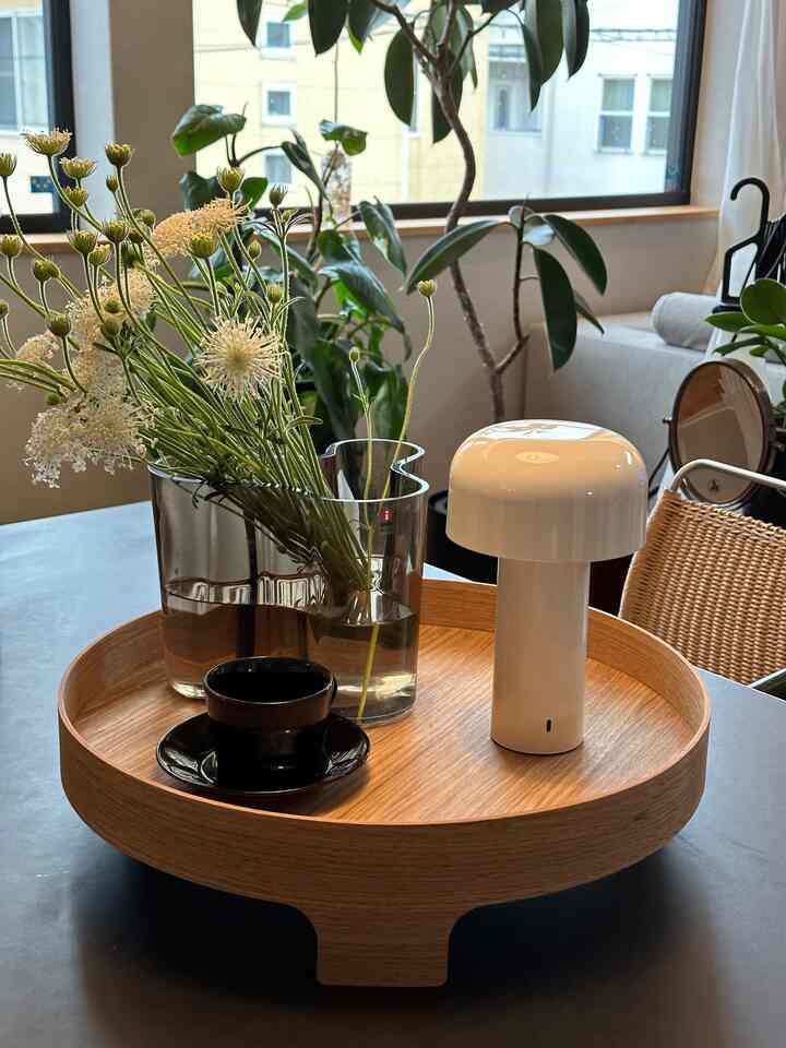 ナチュラルな木目調のトレイに白いテーブルランプ、花の入ったガラス花瓶、黒いティーカップが置かれた北欧スタイルのダイニングスペース