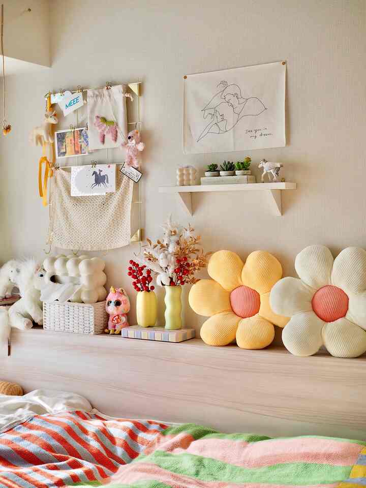 白い壁の寝室、黄色い花形クッションと色彩豊かなブランケットがベッドに配置され、インテリア雑貨が温かみのある雰囲気を演出している