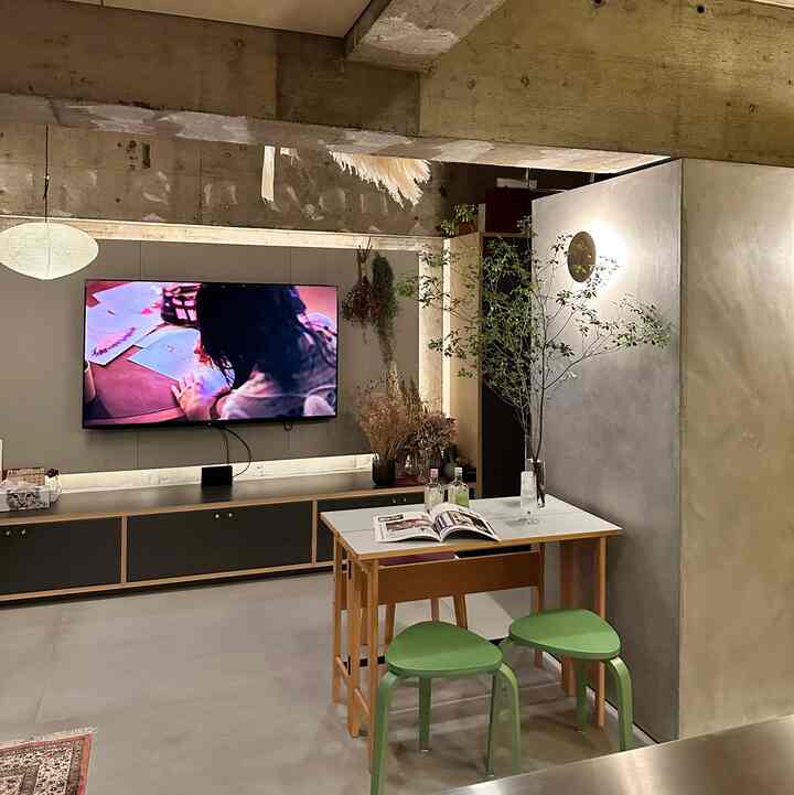 Natural tone studio apartment living room featuring wall-mounted TV, console table, wooden dining table with green stools in a modern interior
