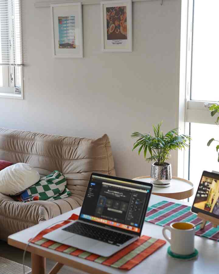 ベージュ色調のリビング、シンプルなソファとデスク上のノートパソコン、グリーン植物が配置された自然なホームオフィスの印象的な空間