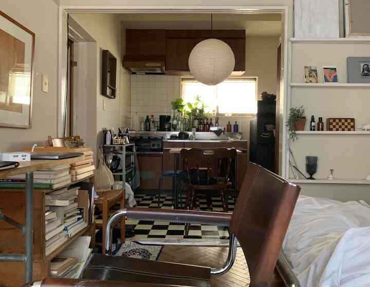 A natural-toned apartment space connecting brown and white kitchen and living area, featuring bookshelves and wooden furniture