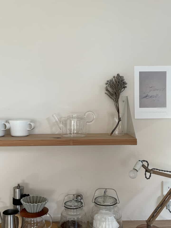 ナチュラルな色調のキッチン壁に木製の棚とコーヒー器具が配置されたシンプルなおうちカフェの空間