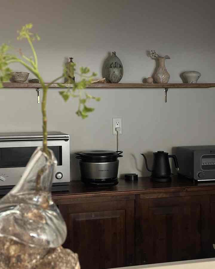 ベージュ調の壁と木製キッチンボードが配されたシンプルなキッチンスペース、棚の上には陶器の飾り物が置かれている