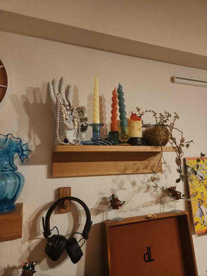 Beige-toned wall featuring an oak wood shelf decorated with colorful twisted candles, a hand-shaped objet, and a potted plant for cozy interior