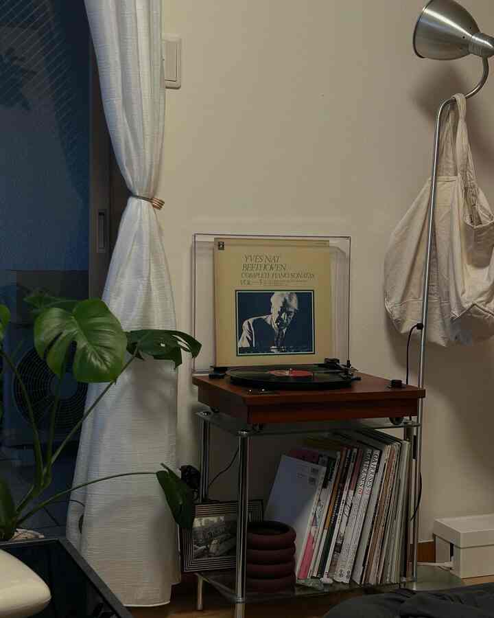 白い壁とカーテンを背景にしたミッドセンチュリーモダンスタイルのリビングコーナー、木製のレコードプレーヤーと観葉植物が配された雰囲気のある空間