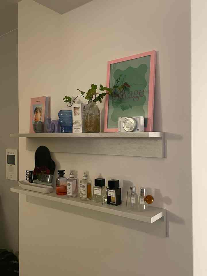 白い壁に取り付けられた二つの棚があり、香水や植物が配置された雰囲気のあるインテリア。