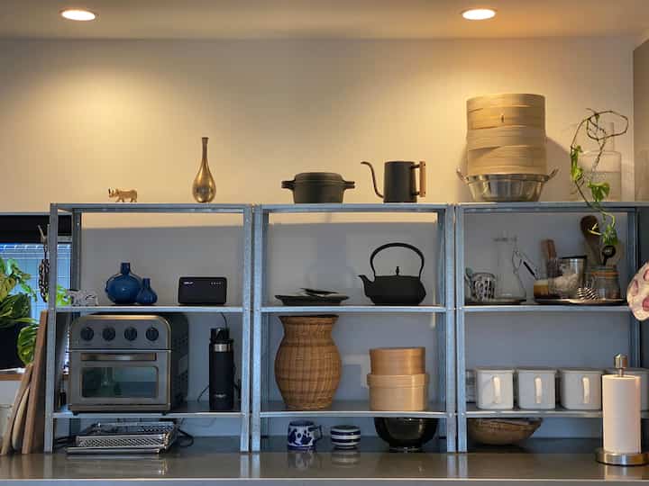 暖色照明の下、白い壁を背景に多様な調理器具と自然素材の装飾が並ぶオープンシェルフのあるキッチン