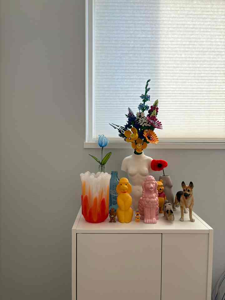 Bright white wall and cabinet adorned with colorful vintage-style vases and a dog figurine, creating a charming decorative display