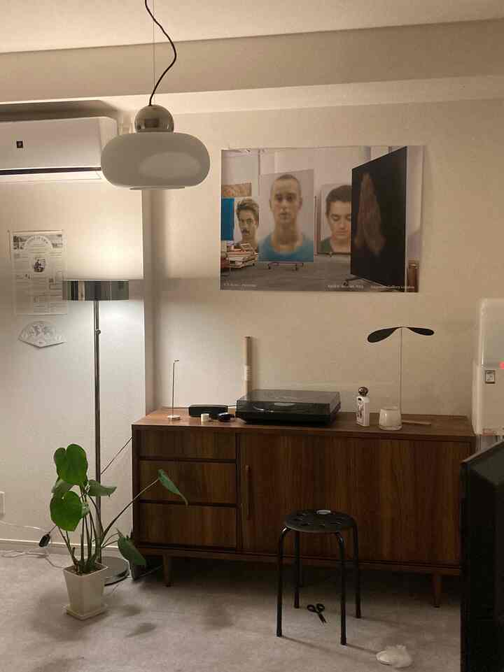 ナチュラルなトーンのブラウン家具と白い壁のリビング、テーブルランプとポスターが配置されたシンプルなインテリア