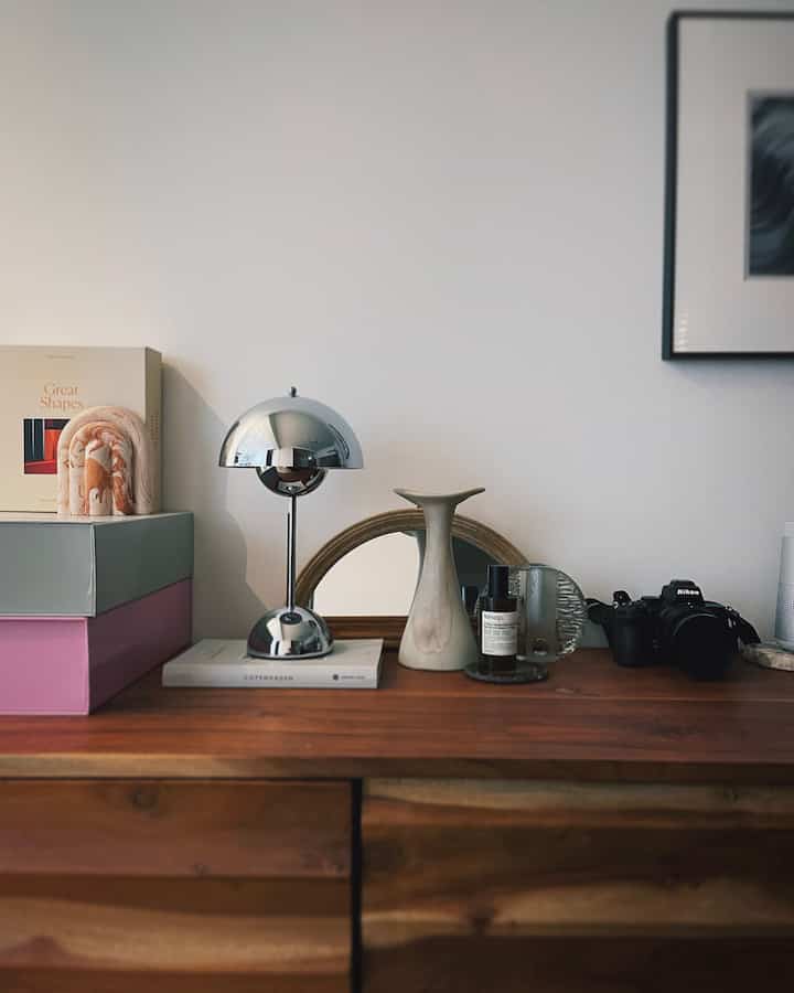 ナチュラルなブラウン木目調のサイドボードにシルバーのテーブルランプと様々なオブジェが配置されたミニマルな空間