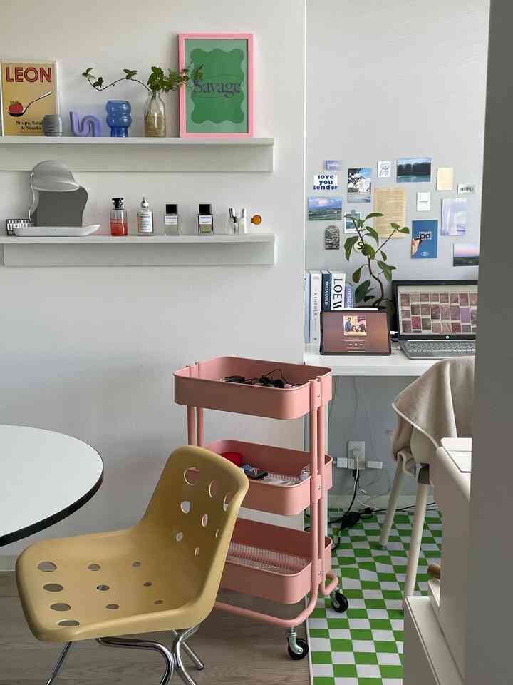 白とピンクを基調としたコンパクトなホームオフィス、黄色い椅子とキッチンワゴンが配置された清潔感のあるインテリア