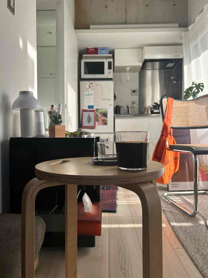 ナチュラルなウッドトーンと白い背景のワンルームキッチンスペース、スツールテーブルと椅子が配置された居心地の良い一人暮らしのホームカフェ風インテリア