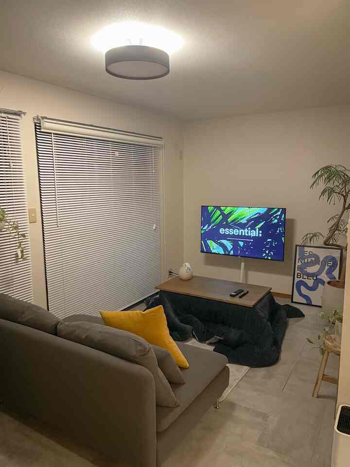 Gray and yellow toned small living room with sofa, kotatsu table, and blinds creating a cozy space