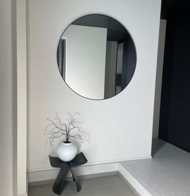 白い壁と黒いスツール、大きな丸い鏡が配置されたモダンな印象の玄関スペース