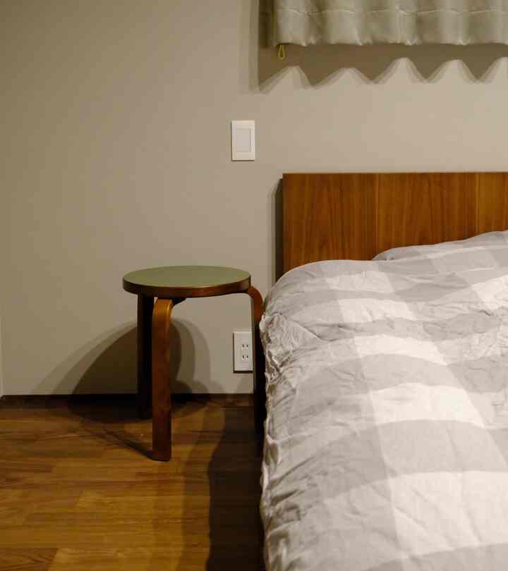 ナチュラルな木目調の床とスツールが置かれた、シンプルで落ち着いた寝室のインテリア