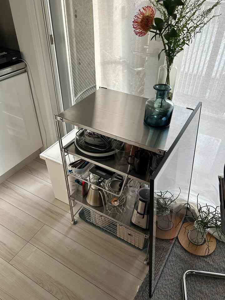 ナチュラルカラーと白を基調としたワンルームのキッチン、ステンレス製ユニット棚とホームカフェのコーヒー用品が配置された印象的なインテリア