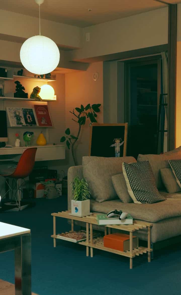 Living room with beige sofa and blue rug, featuring round pendant light, desk, and plants creating a cozy atmosphere