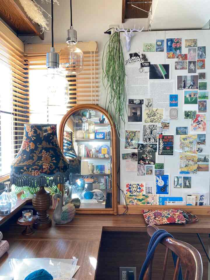 ナチュラルな木目調のデスクとフローラルのテーブルランプ、壁にアートポスターが配された雰囲気のあるワークスペース