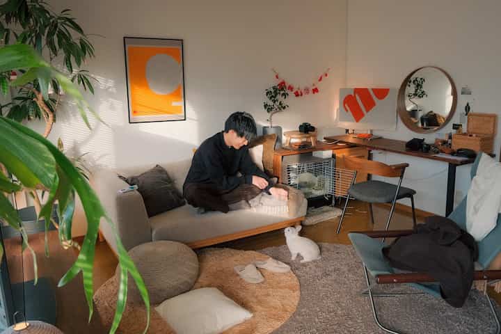 Natural beige-toned 12-tatami living room featuring sofa, armchair, rugs, plants, and a white rabbit creating a cozy atmosphere