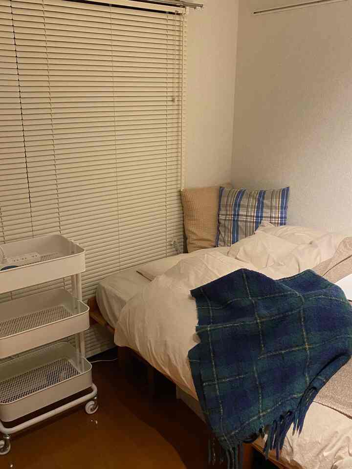 白と木目調の1Kワンルーム寝室、収納トロリーと整った寝具が配置された落ち着いた雰囲気の空間