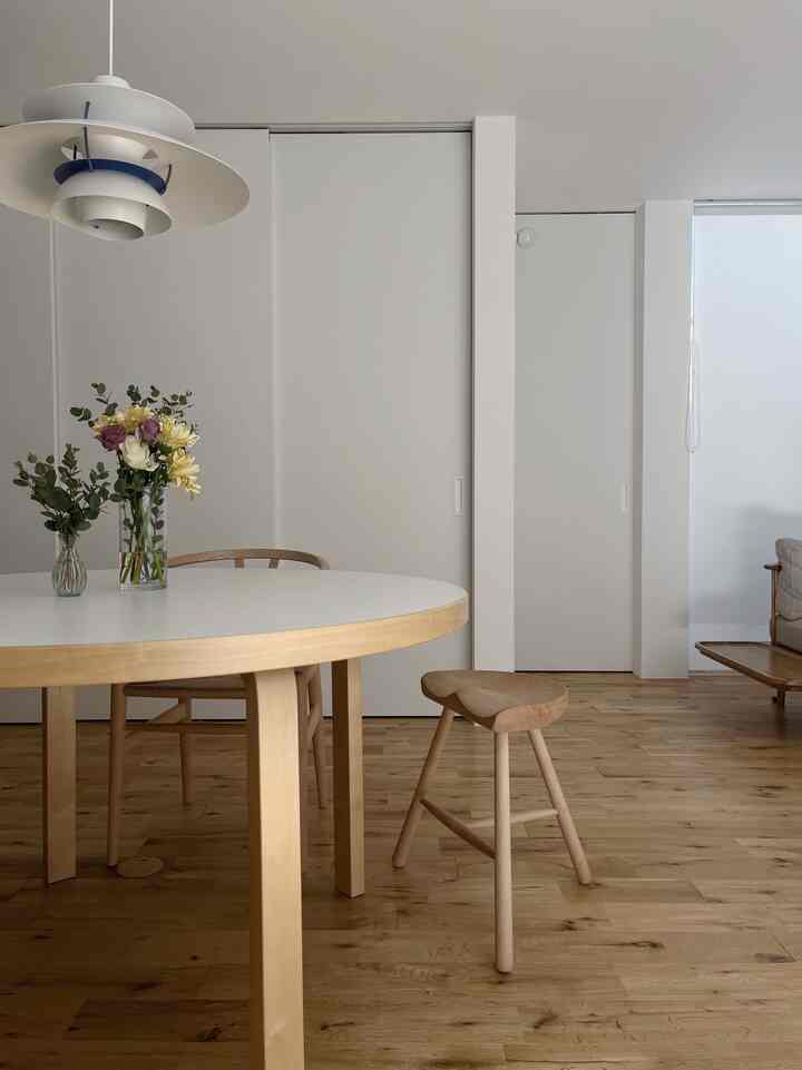 Simple dining room with white walls and wood-tone furniture, featuring a dining table and stool in a tranquil setting