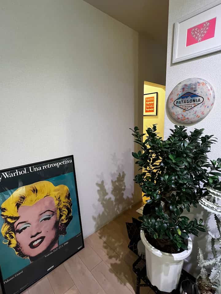 White-walled and beige-floored entrance space featuring framed art, wall decor, and a large potted plant with a clean atmosphere